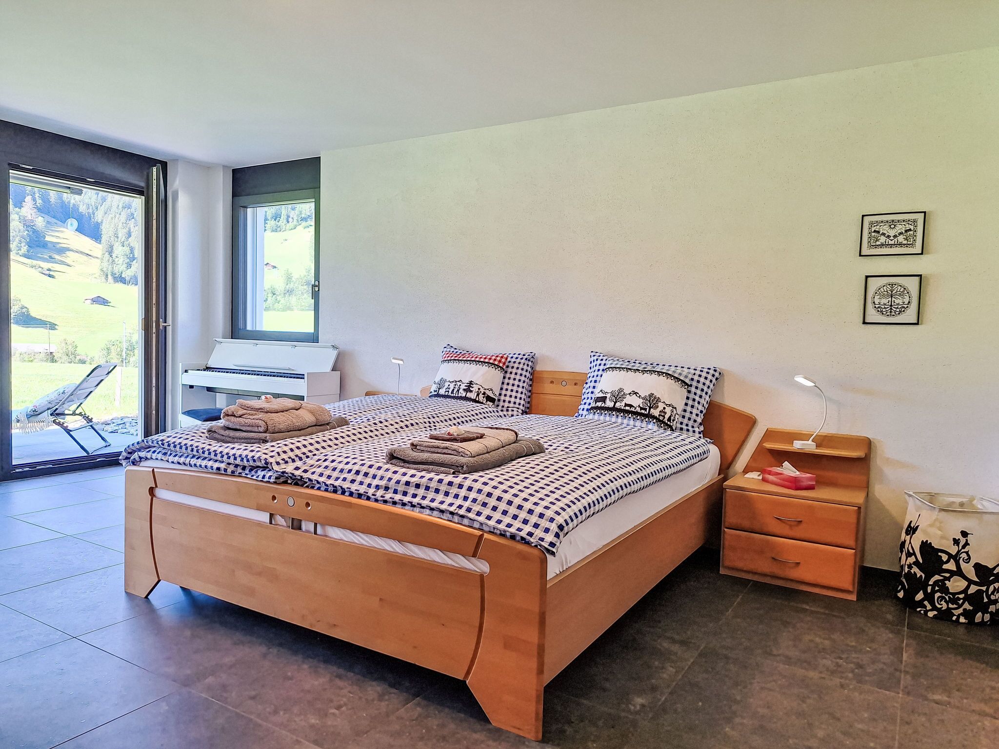 A modern bedroom with a wooden bed, checkered bedding, a piano, and a view of the outdoors.