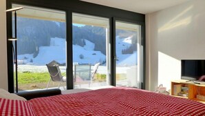 A bedroom with a large bed, a TV, and a view of a snowy landscape through large windows. - Greenview by Interhome (Blankenburg)