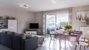 Ein modernes Wohnzimmer mit Sofa, Fernseher und Essbereich mit Stühlen und Tisch.