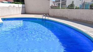 Una piscina azul cristalina con una escalera metálica que da acceso a ella, rodeada de un deck de baldosas y un muro blanco bajo.