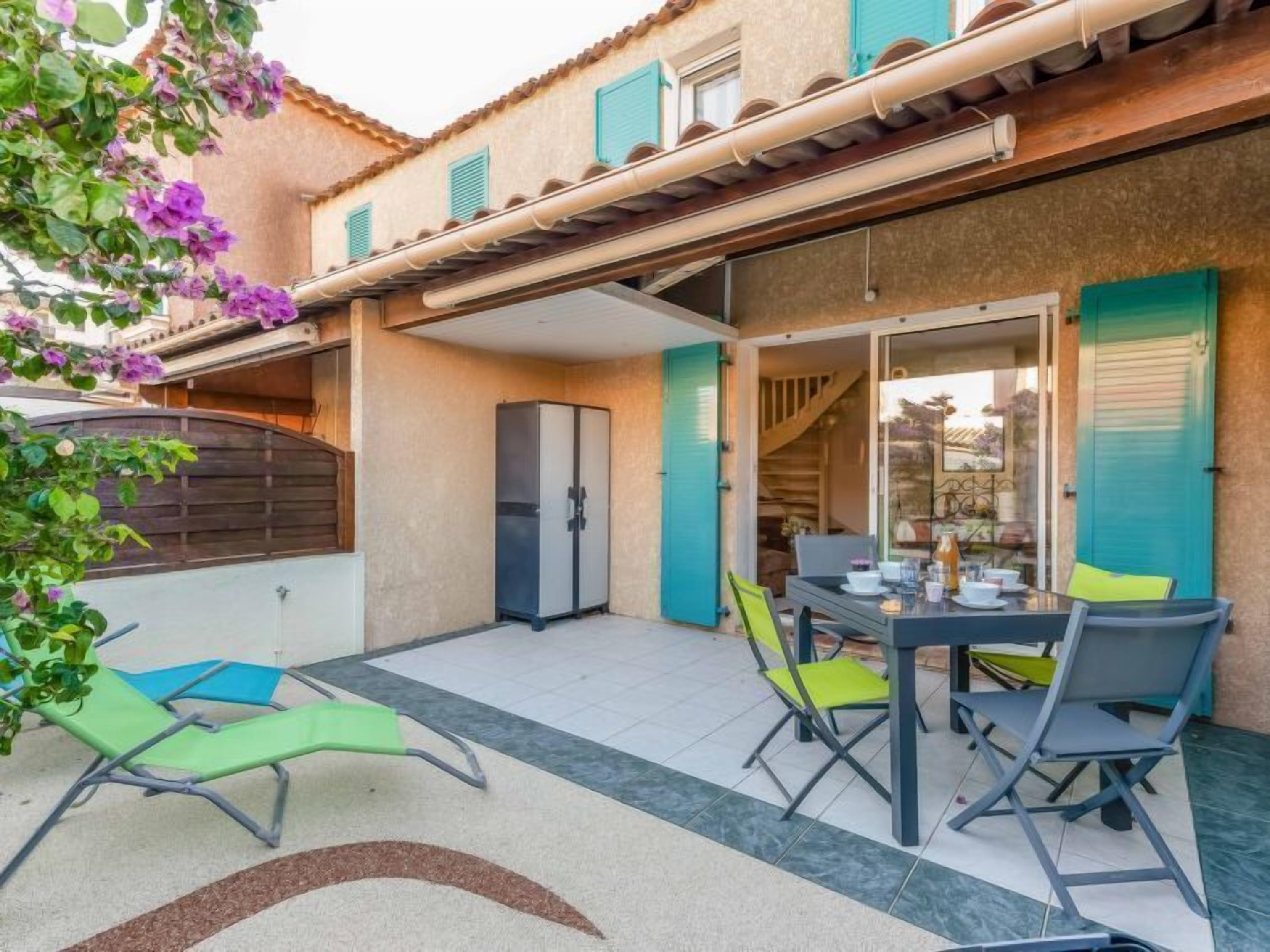 A patio with a table and chairs, a refrigerator, and a covered area with a view of the interior.