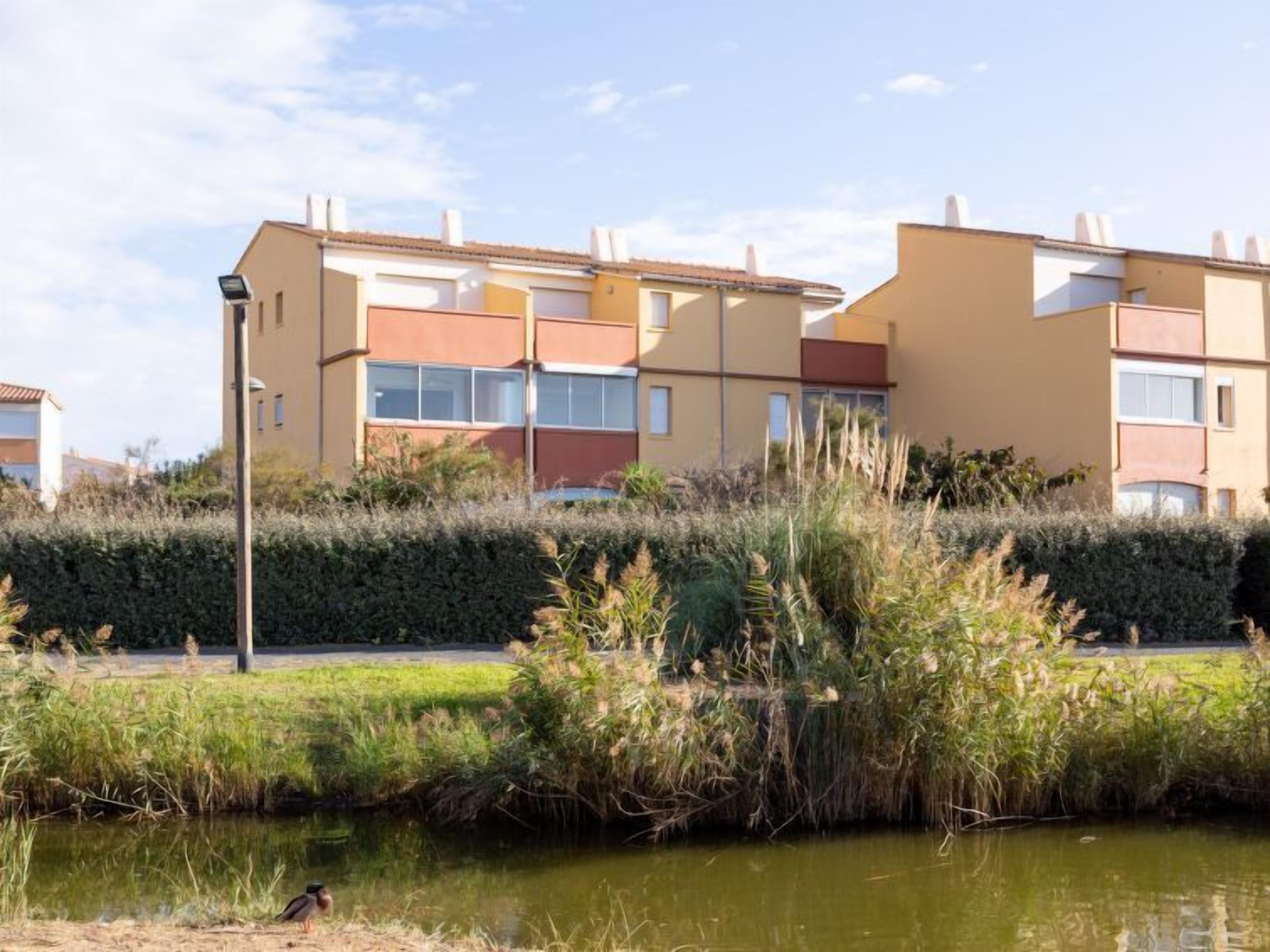 Un immeuble résidentiel doté de nombreux balcons, d’une petite fontaine à l’avant et d’une haie au premier plan.