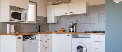 A compact kitchen with white cabinets, a microwave, a coffee maker, and a washing machine.