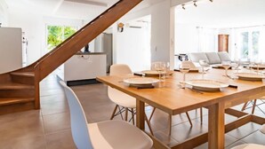 Una cocina moderna con una escalera de madera, un comedor con una gran mesa de madera dispuesta para seis personas, y vistas al exterior.