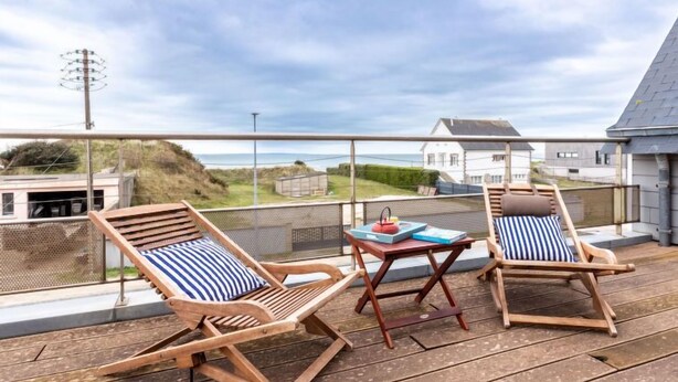 A wooden deck with two lounge chairs and a small table, overlooking a coastal landscape. - La Plage by Interhome (Denneville)