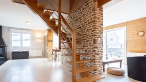 A spacious living area with a wooden staircase, stone wall, and a view of the outside. - La Plage by Interhome (Denneville)