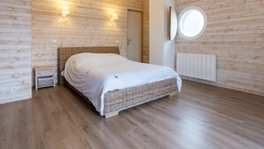 A bedroom with a wooden floor, a bed with a white bedspread, two wall-mounted lights, and a round mirror on the wall. - La Plage by Interhome (Denneville)