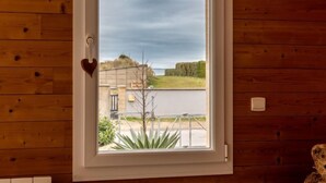 A room with wooden walls, a window with a heart-shaped decoration, and a view of a building and greenery outside. - La Plage by Interhome (Denneville)