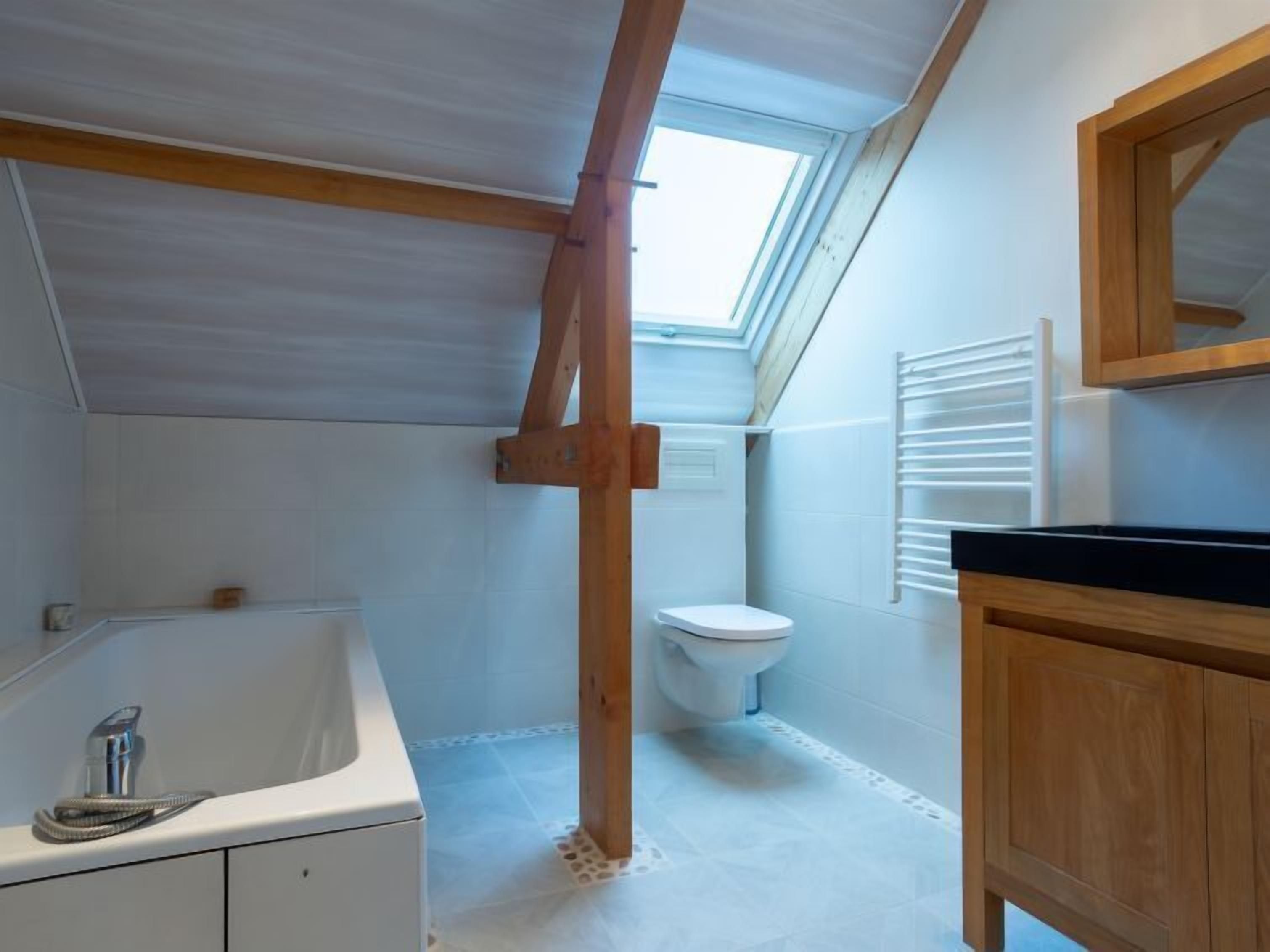 A compact bathroom with a skylight, a bathtub, a toilet, and wooden cabinets.