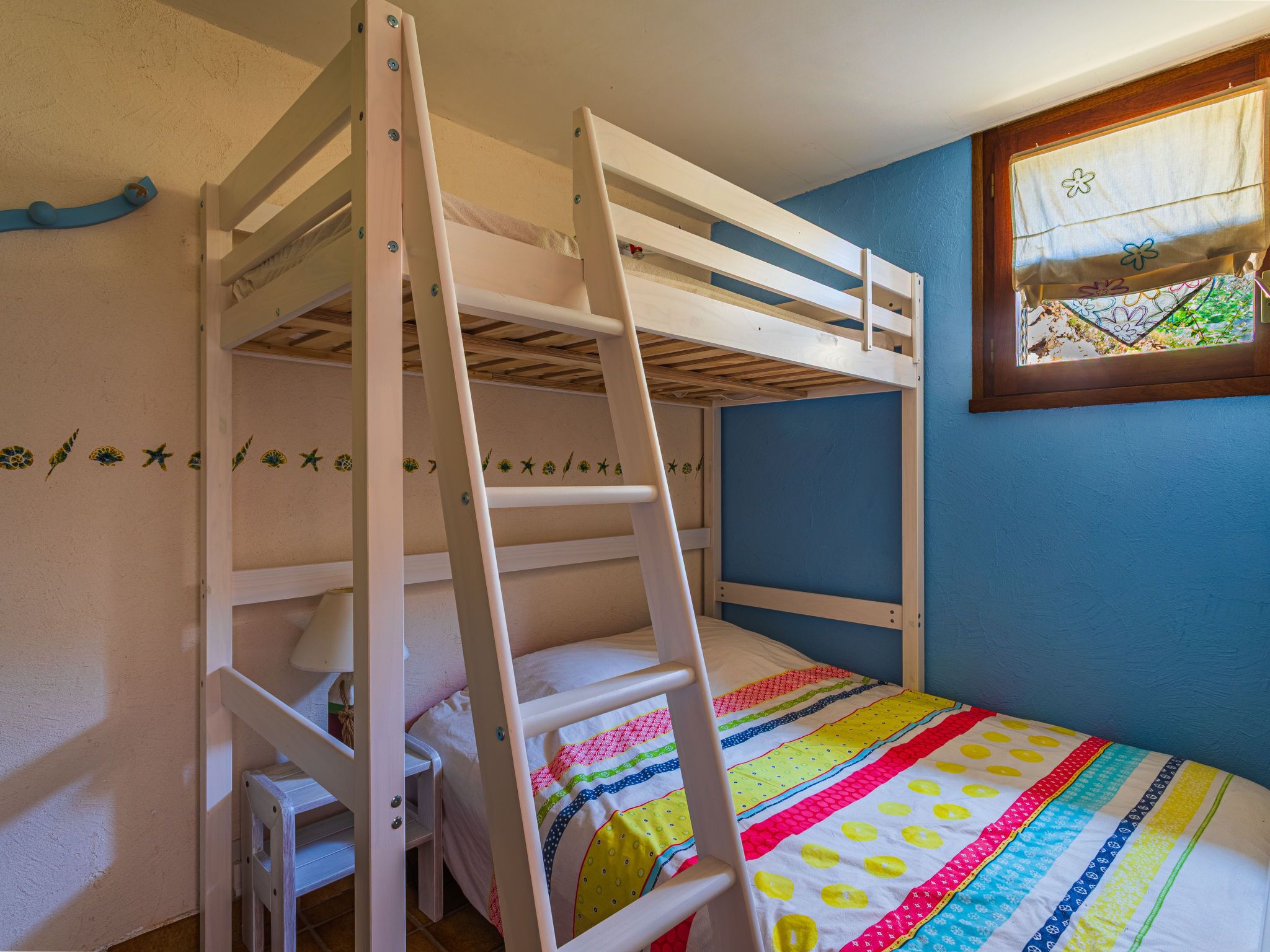 A bunk bed room with a ladder, a window with a view, and a colorful quilt.