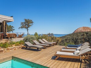 A wooden deck with lounge chairs and a pool, overlooking a coastal landscape.