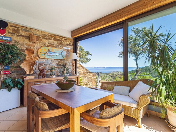 A dining area with a stone wall, wooden furniture, and a view of the sea.