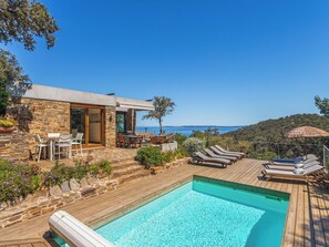 A poolside area with a stone building, outdoor seating, and a view of the sea.