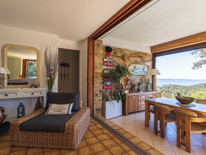 A room with a wicker sofa, a dining table, and a view of the outdoors.