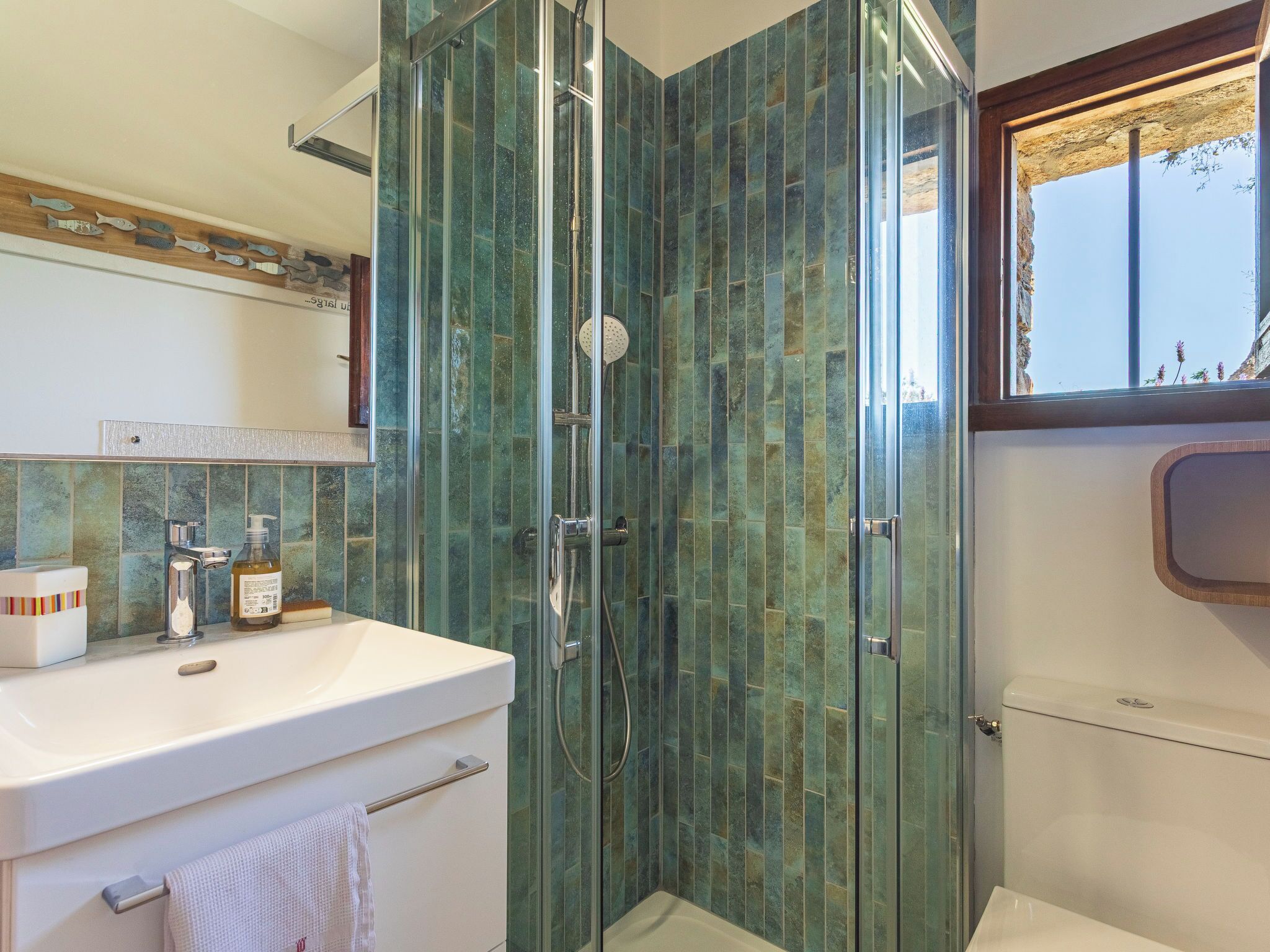 Une salle de bain avec une douche à parois de verre, un lavabo blanc et une fenêtre donnant sur un beau paysage.