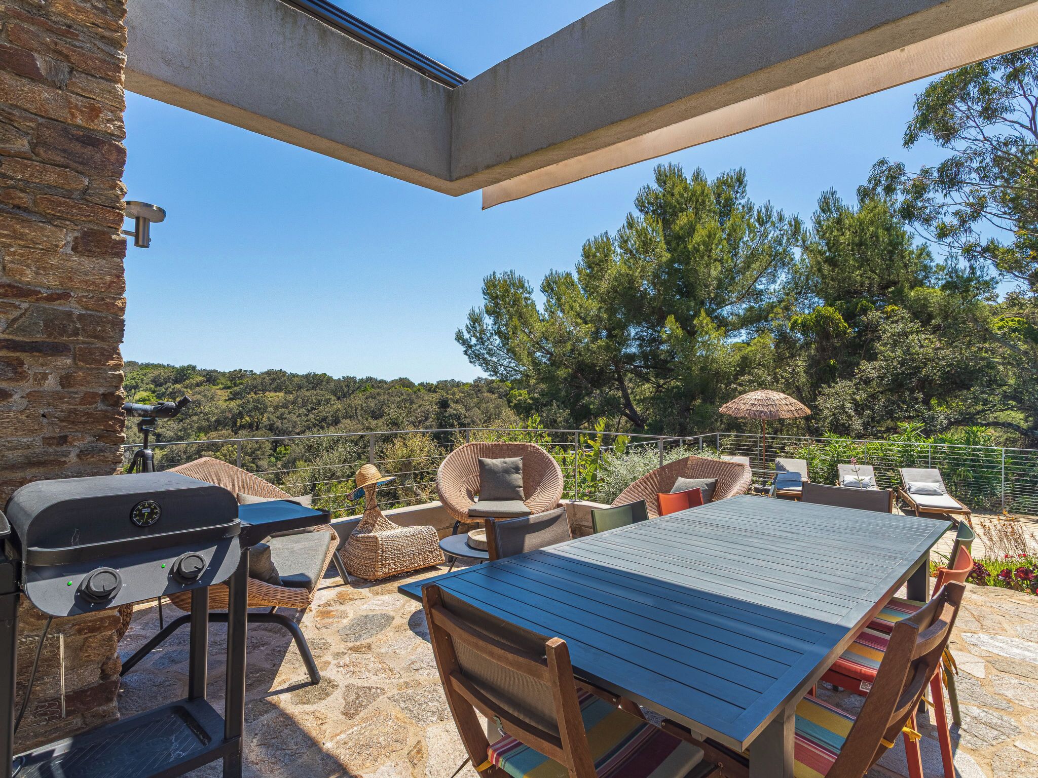 Un patio al aire libre con suelo de piedra, una parrilla, mobiliario de mimbre y una mesa.