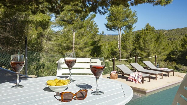 Ein Tisch am Pool mit Weingläsern, einer Obstschale und Sonnenbrillen. Im Hintergrund sind Liegestühle und ein Schwimmbecken zu sehen.