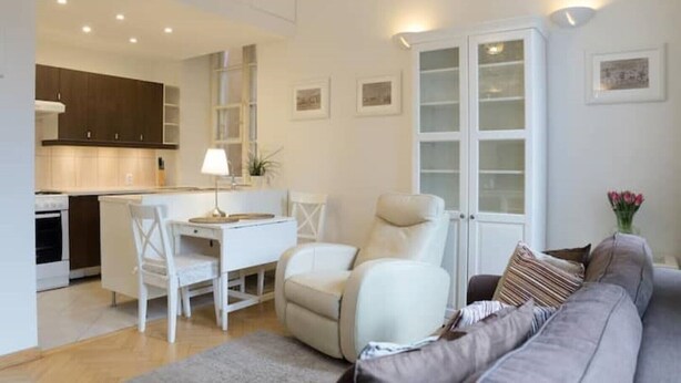 Un salon moderne avec un canapé, un coin repas comprenant une table et des chaises, et une cuisine en arrière-plan.