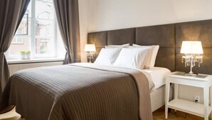 Une chambre d’hôtel avec un grand lit, deux tables de chevet avec des lampes, une fenêtre avec des rideaux et une vue sur les bâtiments environnants.