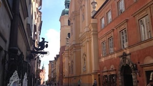 Une rue bordée de bâtiments historiques, dont une église surmontée d’un dôme et un bâtiment rouge aux fenêtres en arc de cercle.