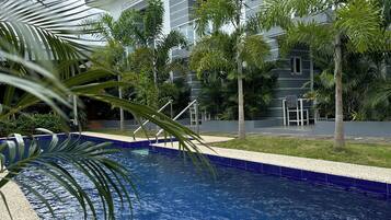 Piscina con un edificio moderno al fondo, rodeada de palmeras.