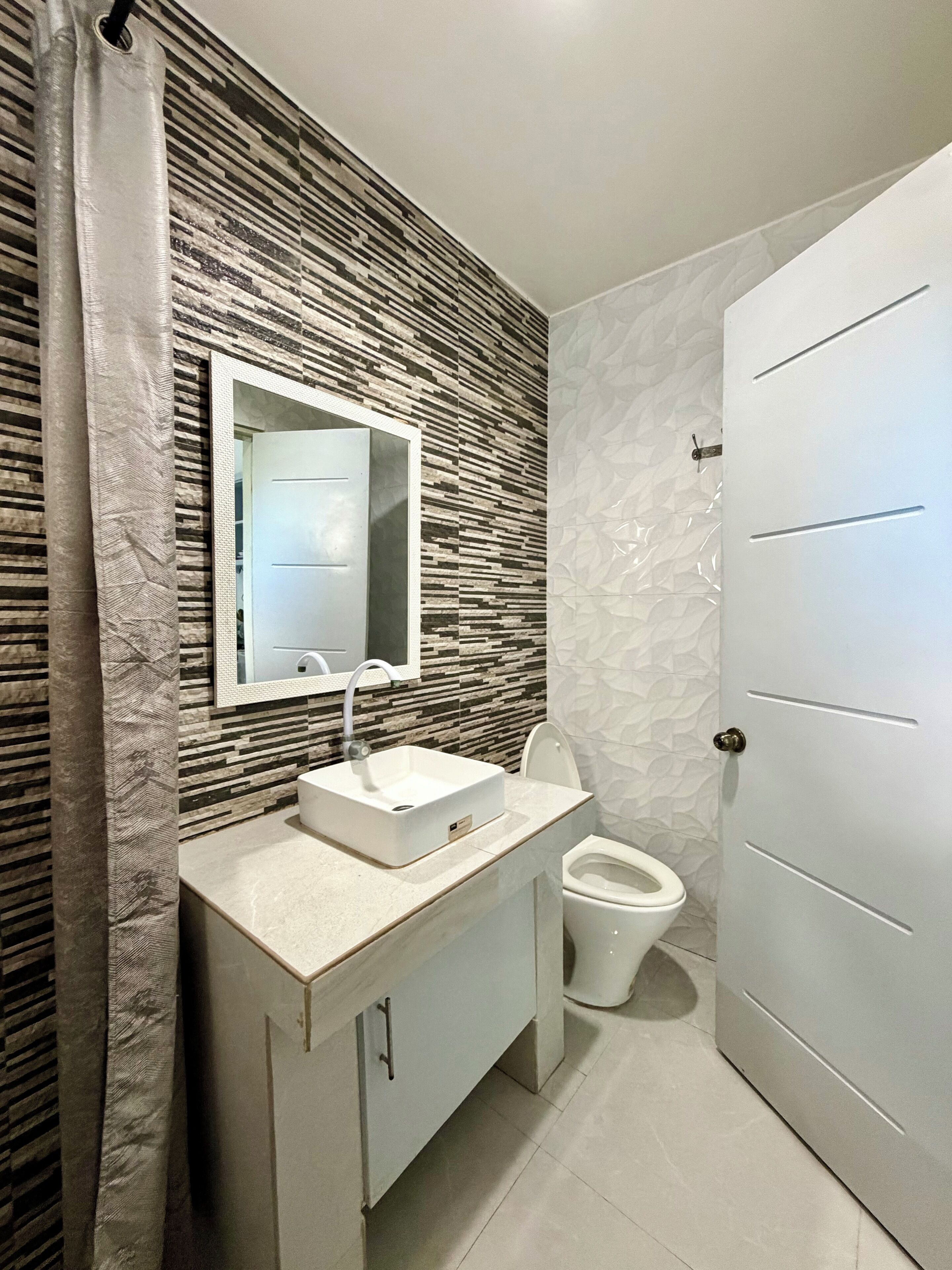 Une salle de bain avec un lavabo blanc, un miroir, des toilettes et une porte.