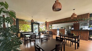 Un ristorante con tavoli e sedie in legno, un bancone con erogatore di acqua e lampade appese in vimini.