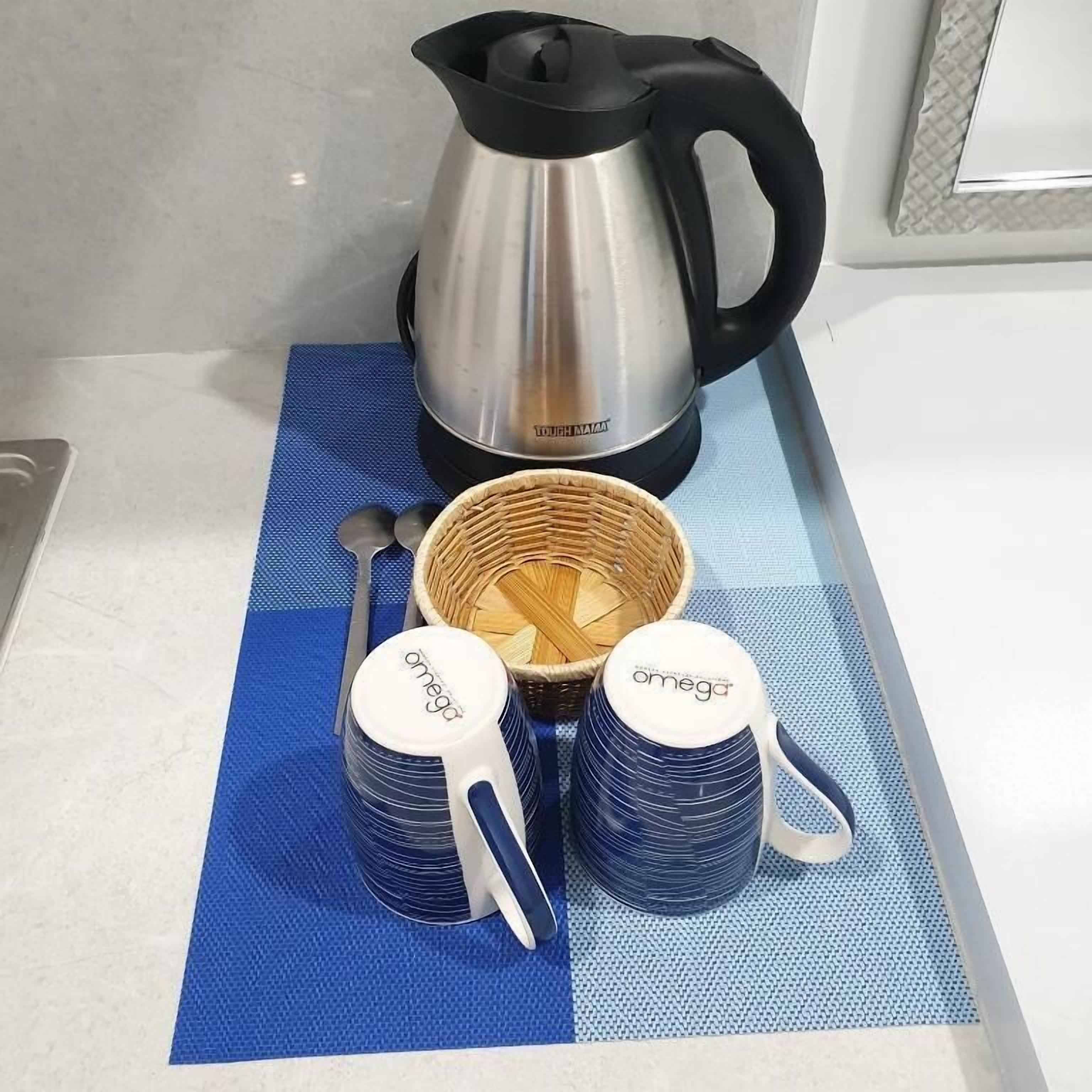 A kitchen counter with a stainless steel kettle, two stacked measuring cups, and a woven basket.