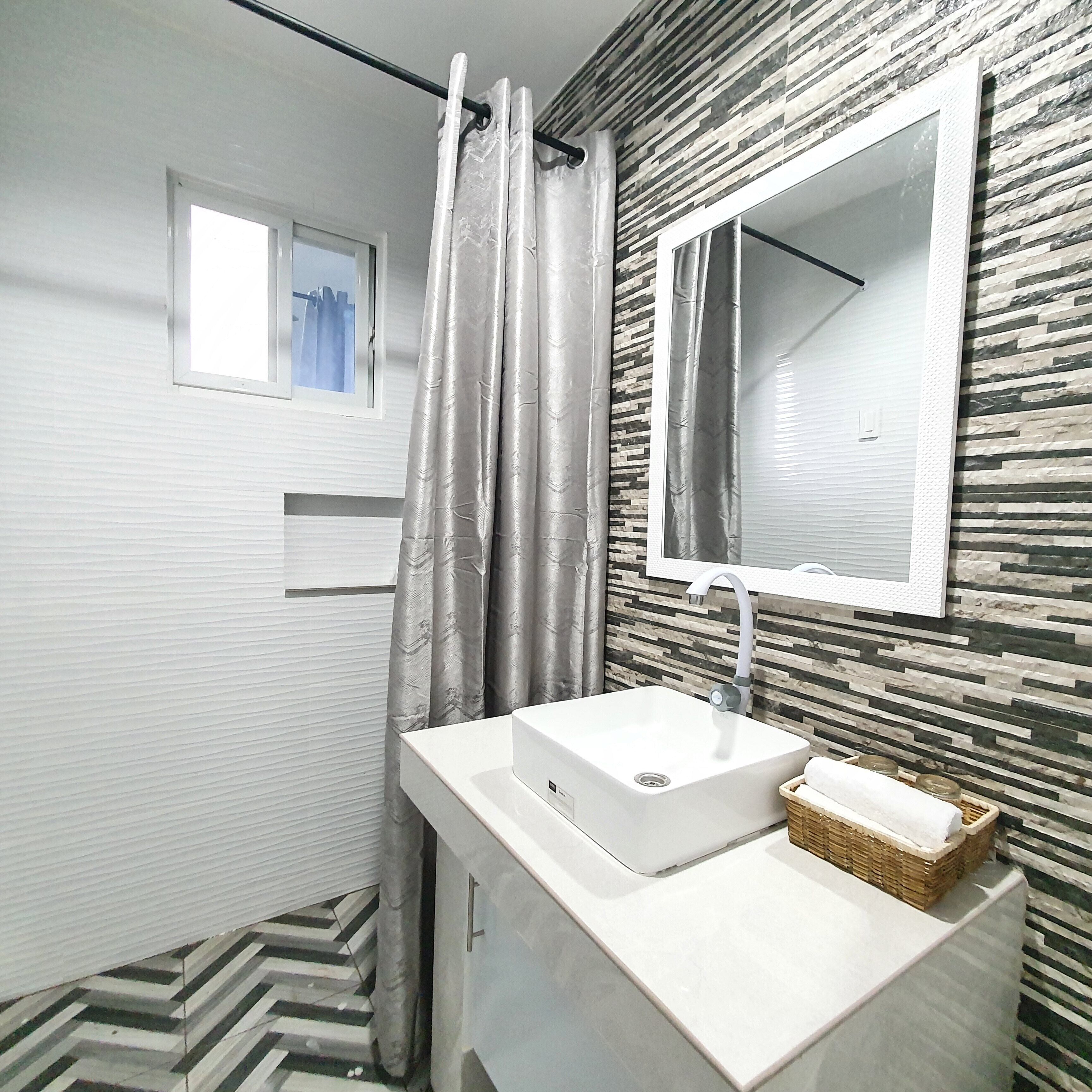 Un baño moderno con un lavamanos blanco, un espejo y una cortina de ducha.