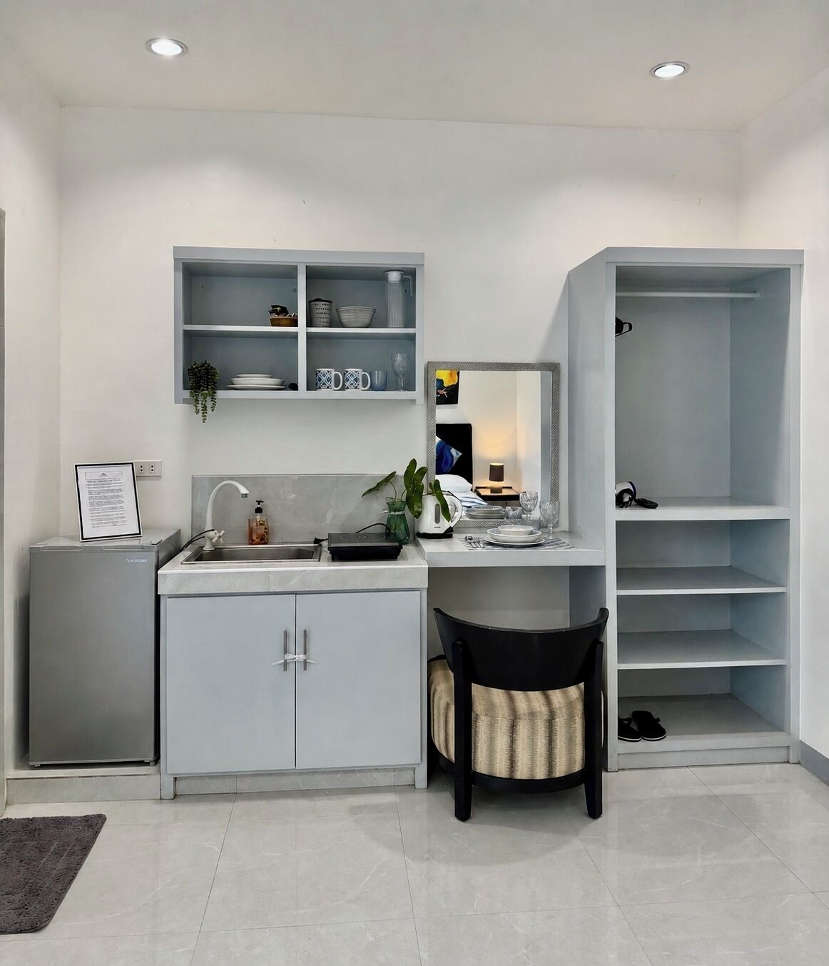 A modern kitchen with a built-in sink, a dining area with a chair, and a white wardrobe with shelves.
