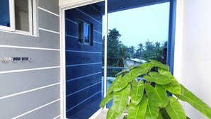Esterno di un edificio moderno con facciata grigia, una grande pianta in vaso e vista su un quartiere residenziale con palme.