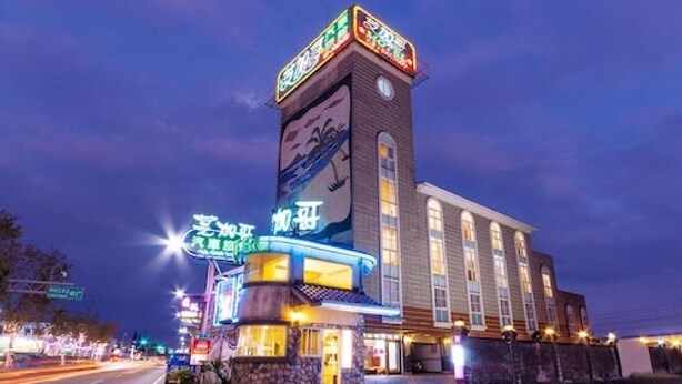 A hotel with a prominent tower featuring illuminated signage, a ground-level entrance with a neon sign, and a large windowed facade. - Chicago Motel (Jiaoxi)