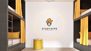 Una stanza moderna con letti a castello, un logo circolare al muro e una piccola botte gialla.