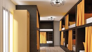 Un corridoio moderno di un hotel con letti a castello, pavimento in legno e una lampada a soffitto geometrica.