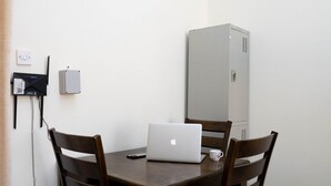 Een eetgedeelte met een houten tafel en stoelen, een laptop, een whiteboard en een klein kastje.