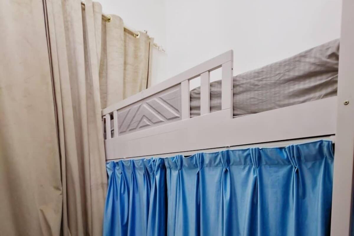 A bunk bed with a blue bed skirt, beige curtains, and a white headboard.