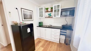 A compact kitchen with white cabinets, a black refrigerator, a microwave, and a sink.