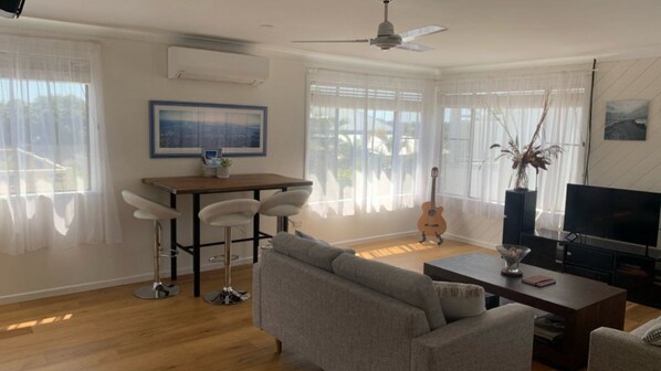 A living room with a sofa, a coffee table, a TV, a guitar, and a dining area with chairs and a table.