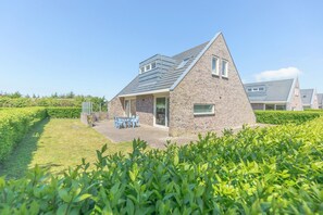 A modern house with a sloped roof, a patio with outdoor furniture, and a well-maintained garden. - A spacious and comfortable house with a fireplace. How far from the beach does it work? (Callantsoog)