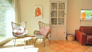 Un saló amb cadires de vimet, un sofà vermell, un armari amb portes de vidre i una finestra amb cortines.