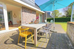 An outdoor patio with a wooden table and chairs, a blue umbrella, and a brick wall. - A spacious and comfortable house with a fireplace. How far from the beach does it work? (Callantsoog)