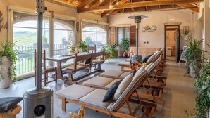 Une pièce spacieuse avec des poutres apparentes, une grande fenêtre et un coin salon agrémenté de coussins et d’une table.