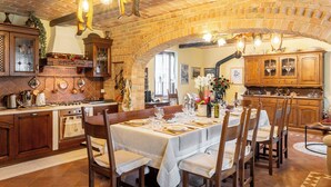 Une cuisine rustique avec des murs en briques apparentes, des meubles en bois et un coin repas avec une table dressée pour six personnes.