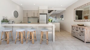 A modern kitchen with a central island, bar stools, and a decorative mirror. - Unit 37 - 2 Bedroom Deluxe Waterfront Townhouse (Noosaville)
