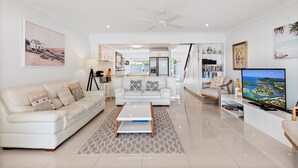 Una sala de estar moderna con un sofá blanco, una mesa de centro y un televisor sobre un mueble.