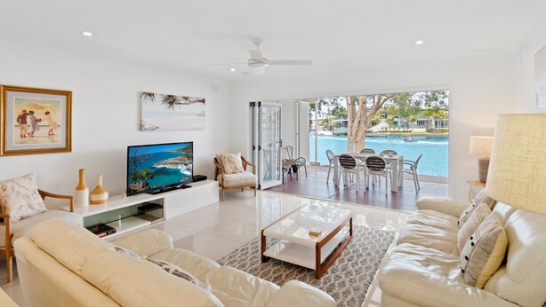 Una sala de estar moderna con televisor, asientos cómodos, una mesa de centro de vidrio y vistas a una piscina y zona exterior.