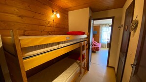Una camera con un letto a castello, pareti in legno e una porta che dà su un'altra stanza.