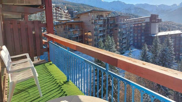 En balkong med utsikt över ett hotellkomplex i ett bergsområde, med flera byggnader och snötäckta träd.