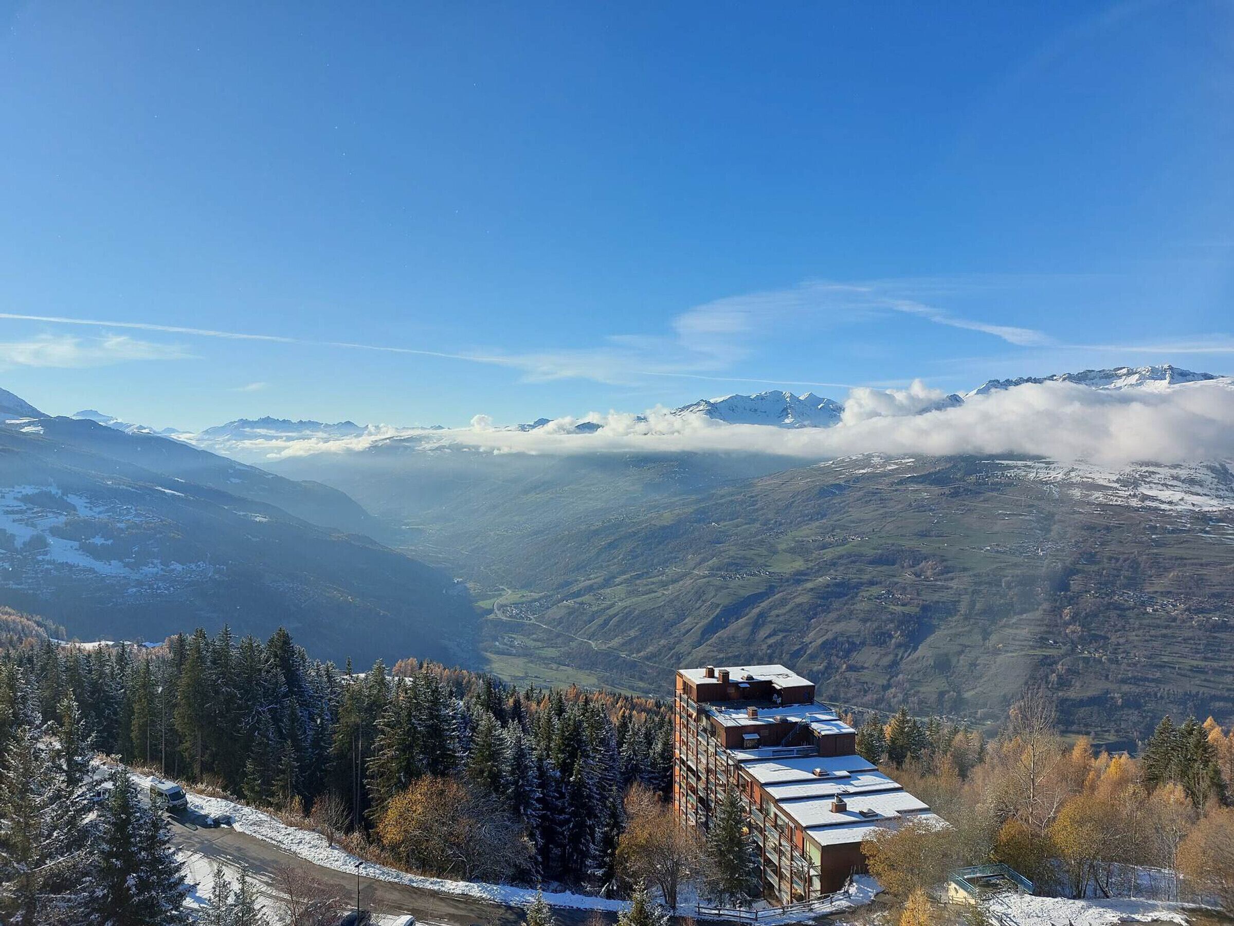 A mountain lodge with a view of snow-capped peaks and a forested valley.