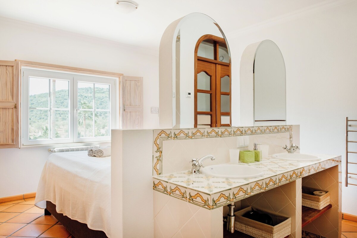 Un dormitorio con cama, ventana y baño con lavabo y espejo.